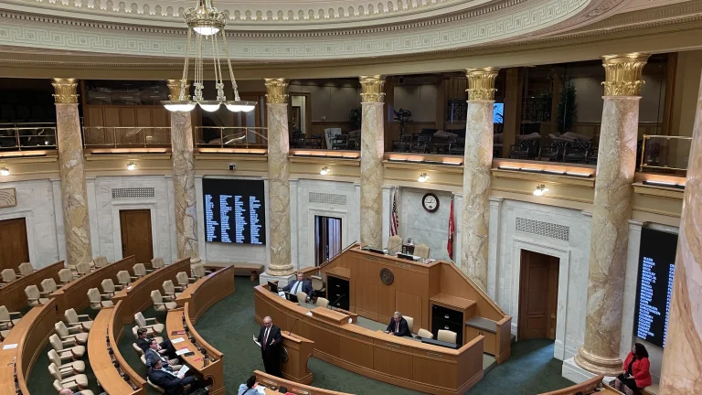 A legislative chamber inside the Arkansas State Capitol, with curved rows of desks under a stained-glass skylight.