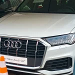 A white Audi Q7 SUV parked at a dealership, front left view.