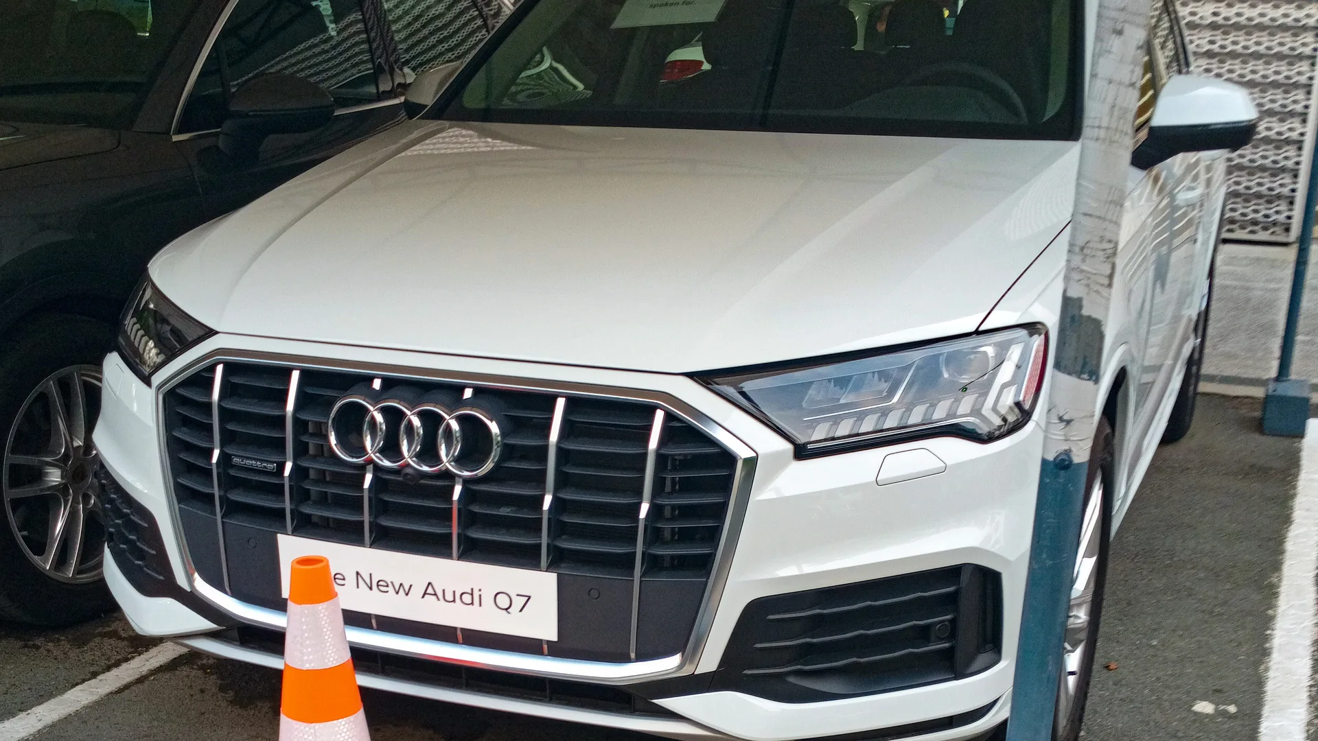 A white Audi Q7 SUV parked at a dealership, front left view.