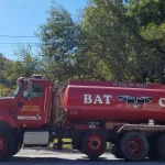 A red Bat Cave Fire and Rescue water tanker truck parked beside a flagpole in Bat Cave, North Carolina, shown as a file photo of a rural volunteer fire department tanker