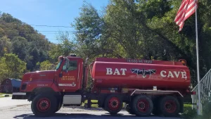 A red Bat Cave Fire and Rescue water tanker truck parked beside a flagpole in Bat Cave, North Carolina, shown as a file photo of a rural volunteer fire department tanker