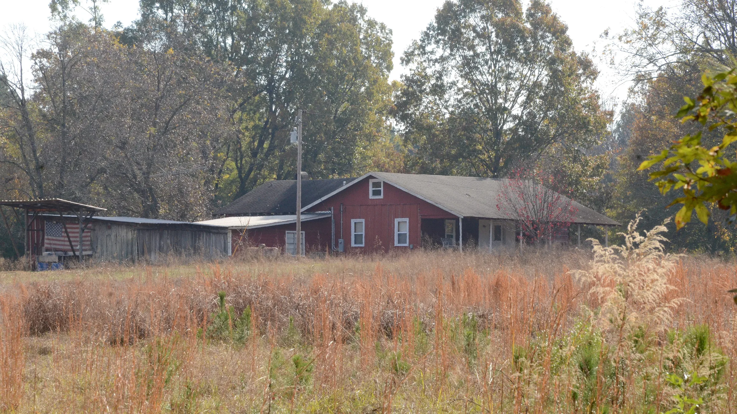 The red Barnett-Attwood House behind a field of tall autumn grass in New Edinburg, Cleveland County, Arkansas.