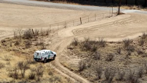 A U.S. Border Patrol truck drives a dirt road in the Arizona desert below the border fence
