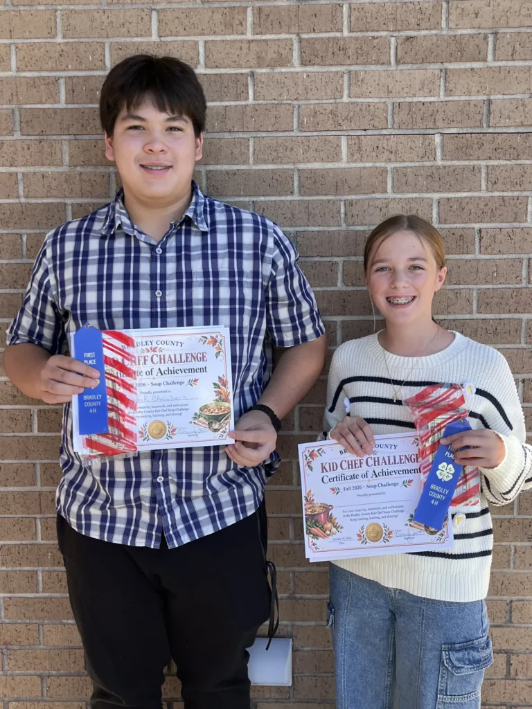Two Kid Chef Challenge participants hold their certificates of achievement and blue ribbons.
