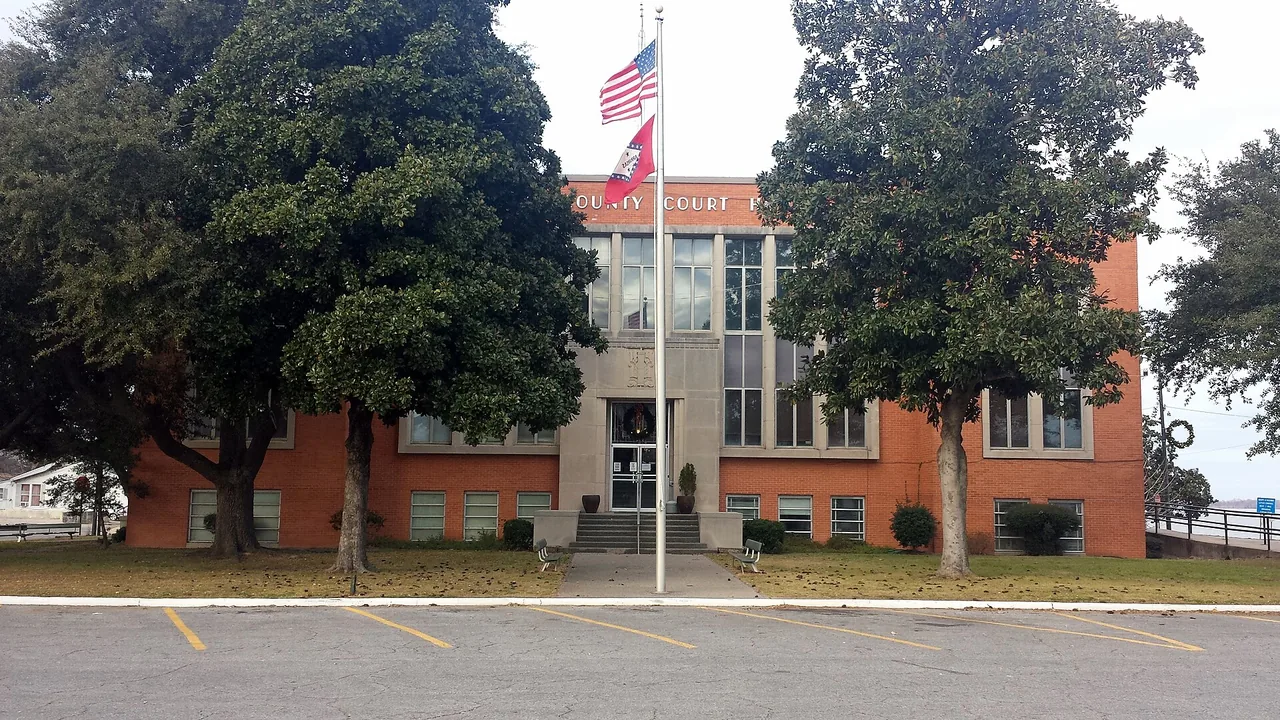 The Chicot County Courthouse in Lake Village, Arkansas, a red-brick building behind large trees with flags out front