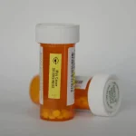 Two orange prescription pill bottles with white caps, one standing and one on its side, against a plain white background.