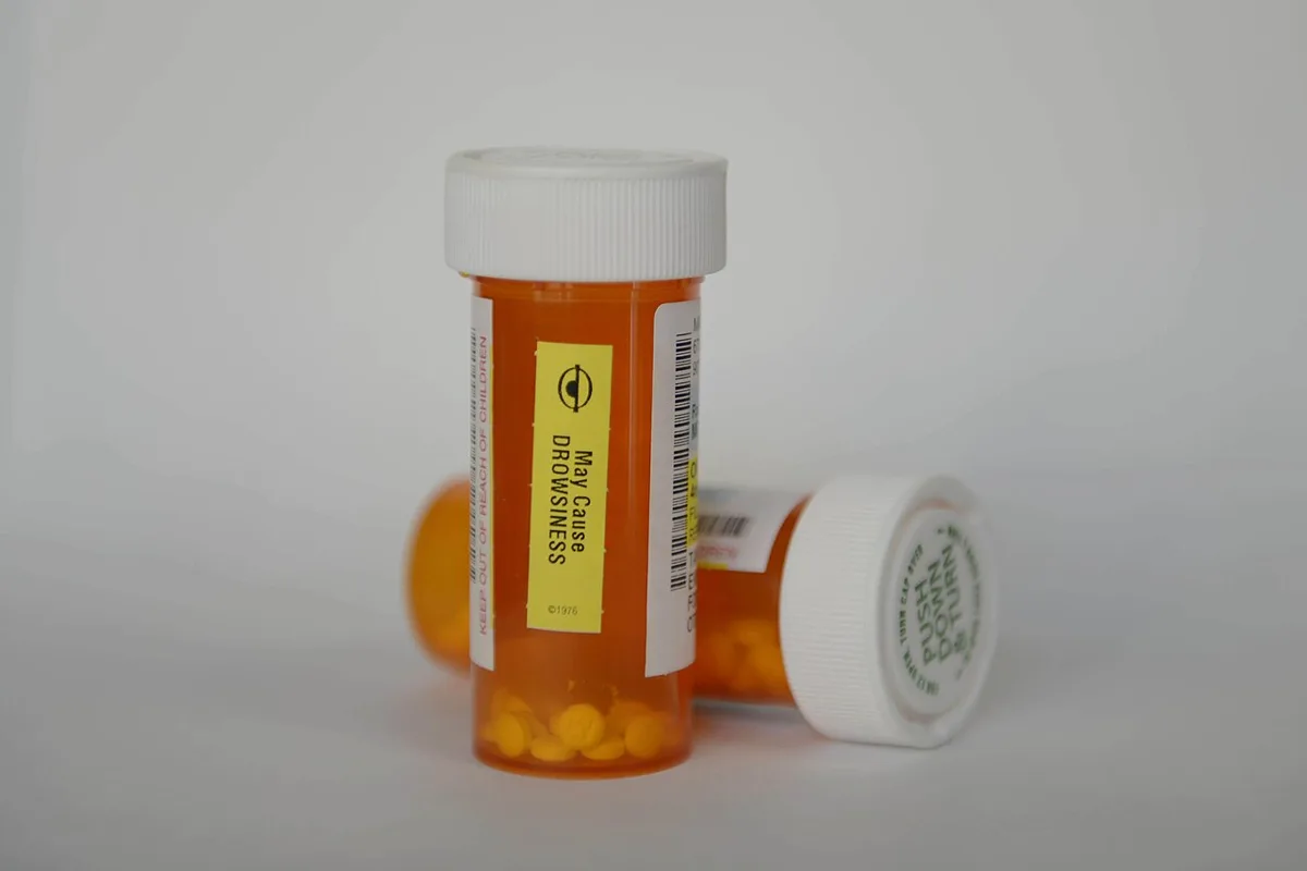 Two orange prescription pill bottles with white caps, one standing and one on its side, against a plain white background.