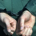 Close-up of a person's hands held behind the back in metal handcuffs