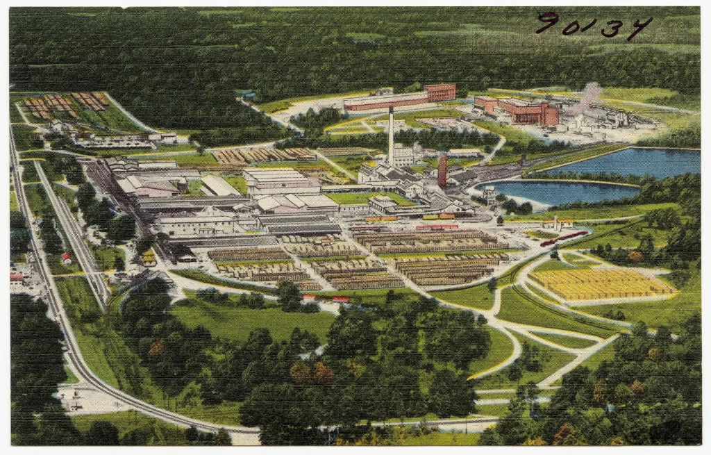 Color linen postcard with a bird's-eye view of a large mill complex with smokestacks, long sheds, stacked lumber yards and rail lines beside two ponds, surrounded by green woods. The number 90134 is handwritten at the top right.