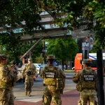 National Guard soldiers in camouflage and vests marked National Guard stand on a brick plaza outside the Eastern Market Metro station in Washington, D.C., during a September 2025 patrol.