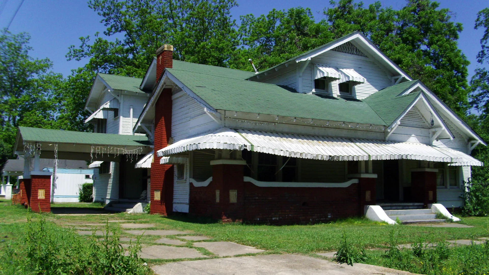 The historic M.E. Davis House in Dermott, a white house with a green roof and red awnings.