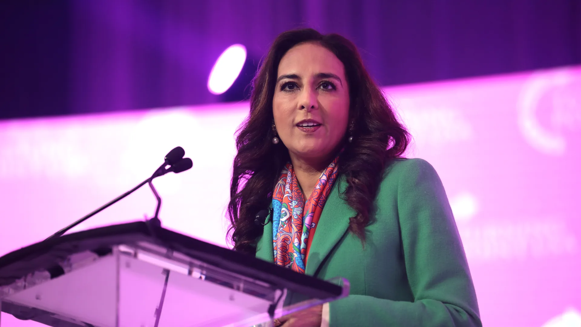 Harmeet Dhillon speaking at a lectern in a green jacket at a 2021 event in Grapevine, Texas