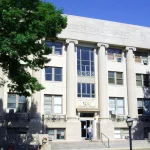 Front of the Drew County Courthouse in Monticello, Arkansas, with tall columns, trees on both sides and a person on the front steps