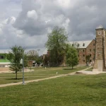 The Centennial Clock Tower and central quad on the University of Arkansas at Monticello campus, with brick and green-trimmed buildings behind a wide lawn.