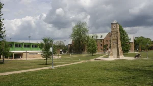 The Centennial Clock Tower and central quad on the University of Arkansas at Monticello campus, with brick and green-trimmed buildings behind a wide lawn.