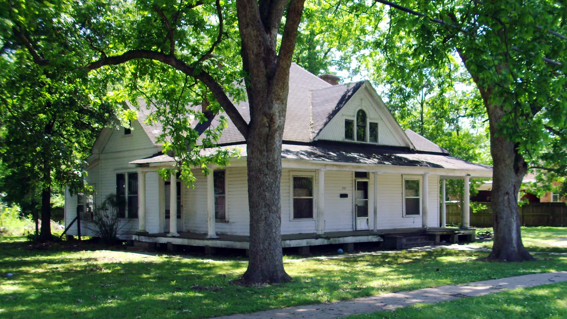 The historic Dr. J.D. Watts House in Dumas, a white two-story frame house with a wraparound porch under large shade trees.
