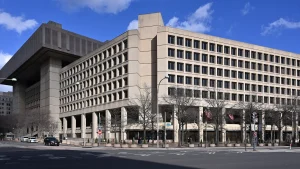 The tan concrete J. Edgar Hoover Building, headquarters of the FBI, seen from across Pennsylvania Avenue in Washington under a blue sky.