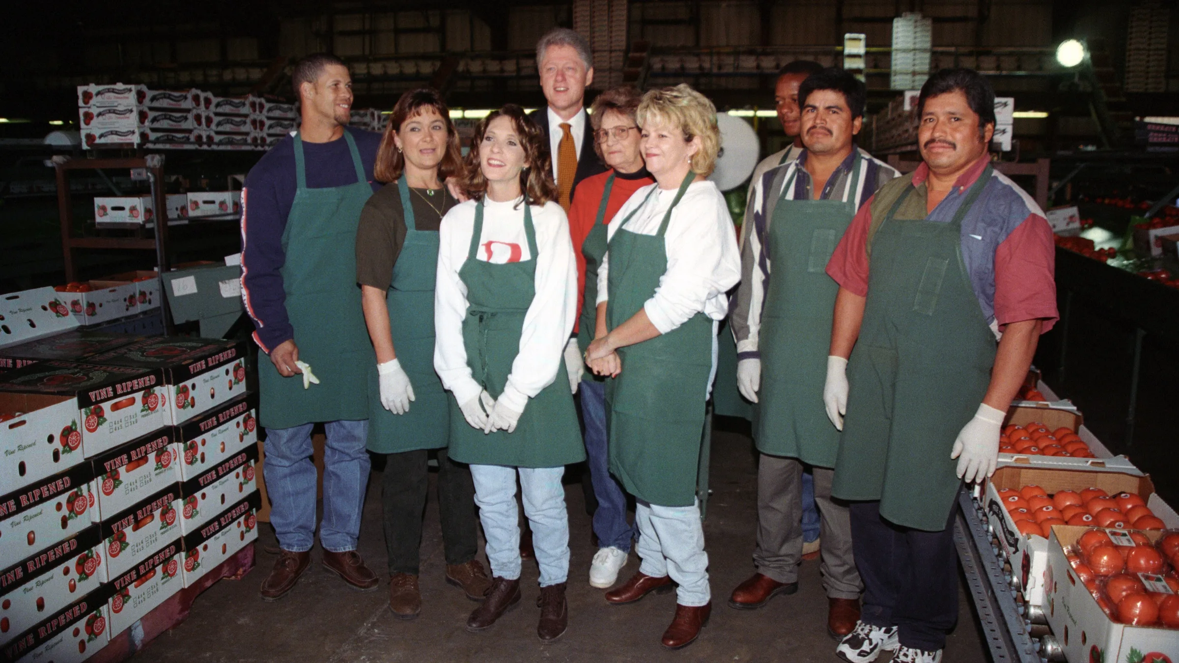 Workers in green aprons at the Hermitage Tomato Cooperative packing shed in Hermitage, Arkansas, during a 1990s presidential visit.