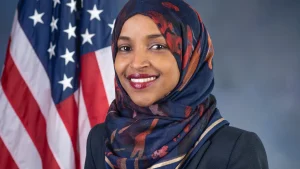 Official 2018 U.S. House portrait of Rep. Ilhan Omar of Minnesota standing in front of an American flag