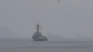 A U.S. Navy guided-missile destroyer sails through haze in the Strait of Hormuz as a helicopter flies overhead
