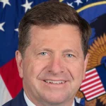 Official portrait of Director of National Intelligence Jay Clayton in front of an American flag and the intelligence office seal.