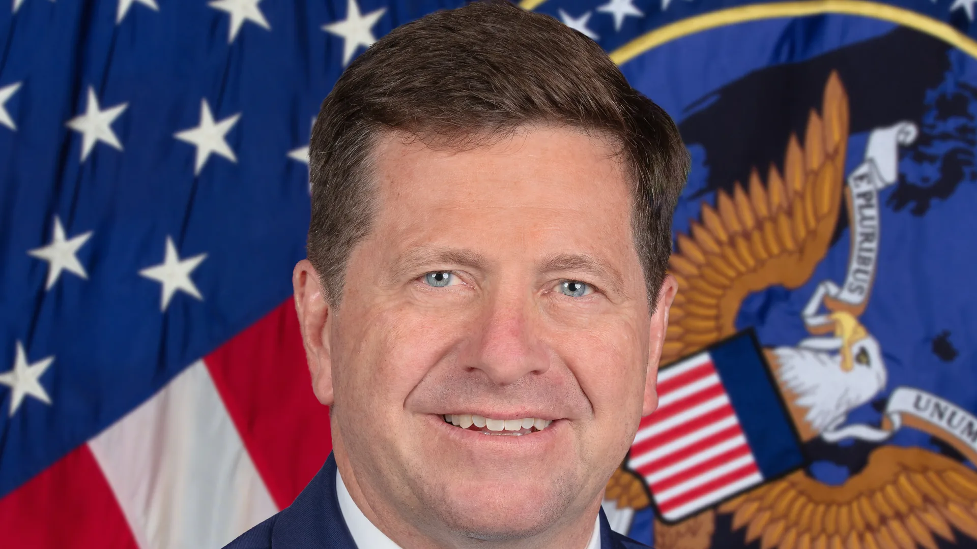 Official portrait of Director of National Intelligence Jay Clayton in front of an American flag and the intelligence office seal.