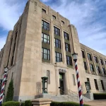 The historic limestone U.S. Post Office and Federal Building in downtown Wichita, Kansas, which houses the U.S. Courthouse, with an American flag and striped lamp posts out front.