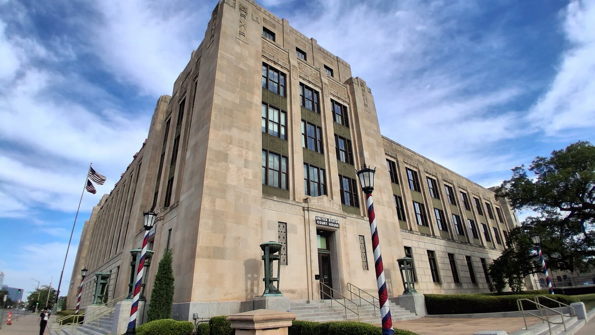 The historic limestone U.S. Post Office and Federal Building in downtown Wichita, Kansas, which houses the U.S. Courthouse, with an American flag and striped lamp posts out front.