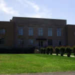 The Lincoln County Courthouse in Star City, Arkansas, a flat-roofed brick building behind a lawn and a row of shrubs