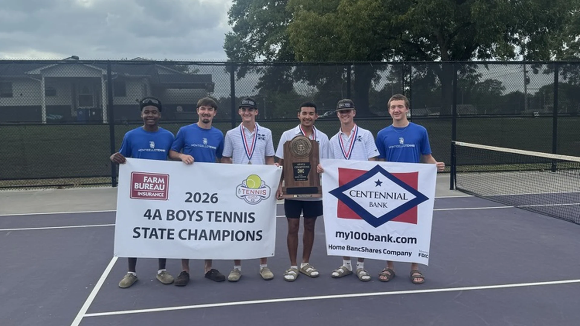 Monticello High School boys tennis players hold a 2026 4A Boys Tennis State Champions banner and a state trophy on a tennis court.