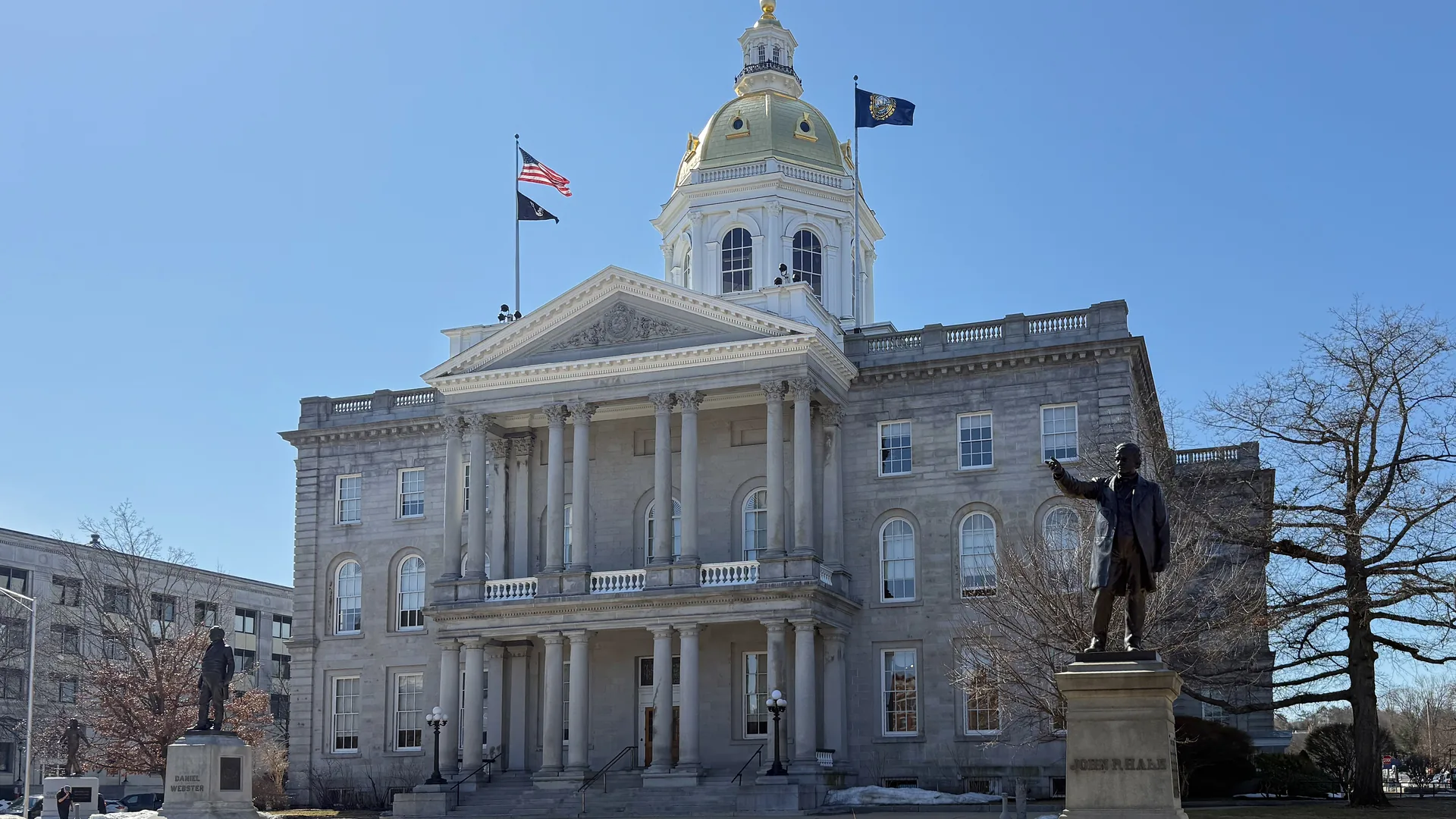 The New Hampshire State House, a granite building with a gold dome and columned portico, in Concord on a clear day.