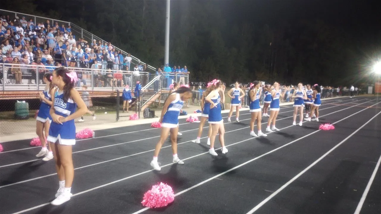 Monticello cheerleaders in blue and white perform on the track in front of the grandstand.