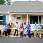 Group cutting a ribbon in front of a new single-story home with blue shutters, built with a USDA Rural Development direct home loan in North Carolina.