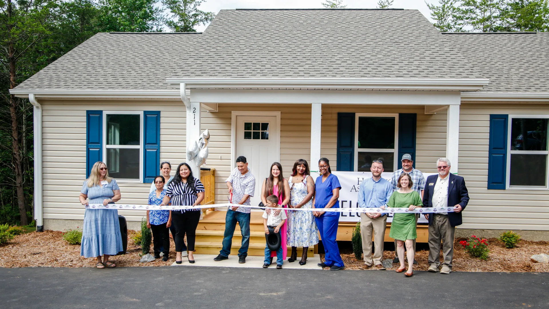 Group cutting a ribbon in front of a new single-story home with blue shutters, built with a USDA Rural Development direct home loan in North Carolina.