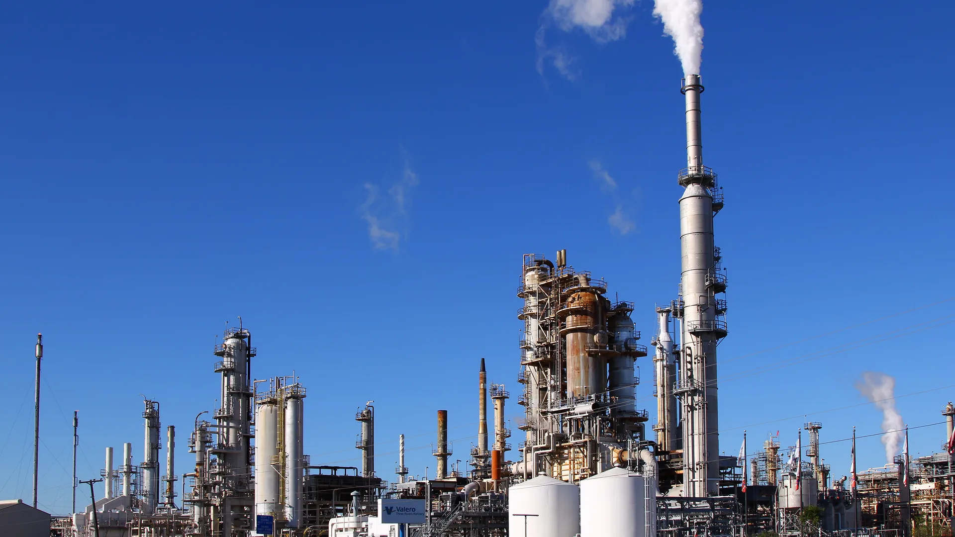 The Valero oil refinery in Three Rivers, Texas, with distillation towers, storage tanks and a tall smokestack under a blue sky.