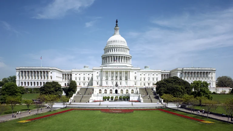 The west front of the U.S. Capitol in Washington under a blue sky, with the dome above the lawn.