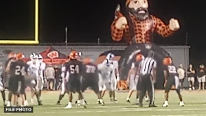Players in black and orange and in white set at the line of scrimmage at night, with an official nearby and a large inflatable lumberjack behind the end zone, marked File Photo