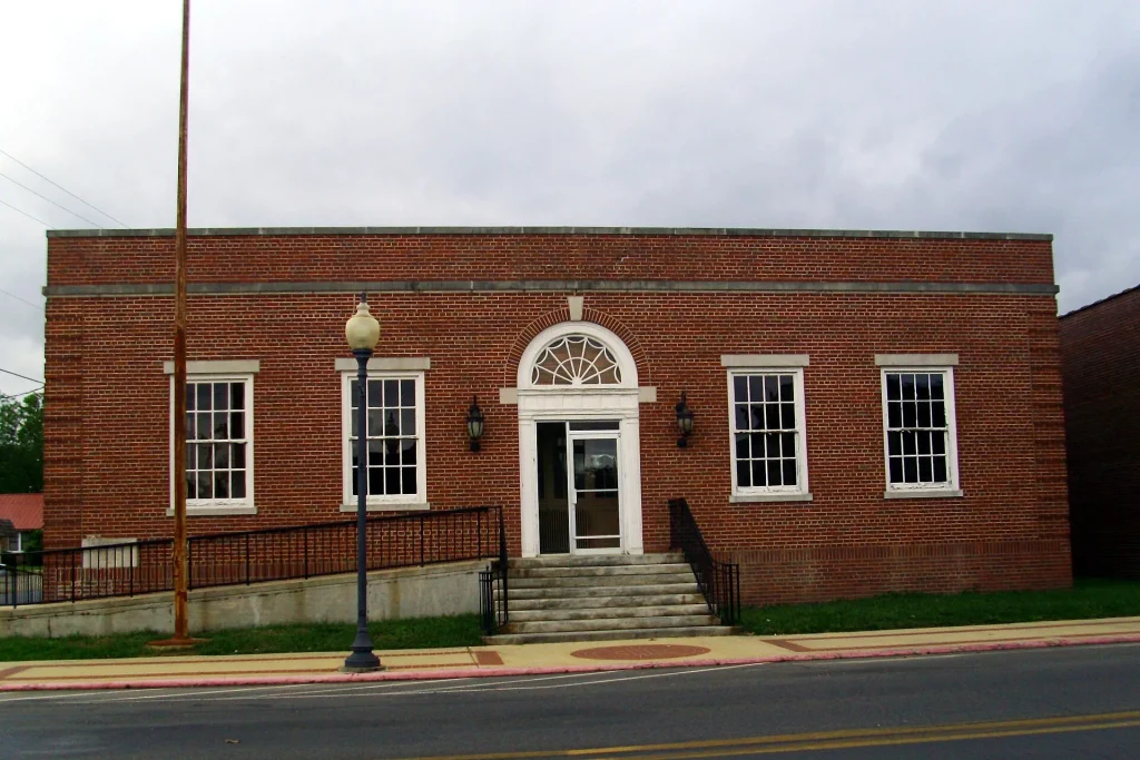 One-story red brick post office with a centered arched doorway, white-trimmed windows and front steps with railings.