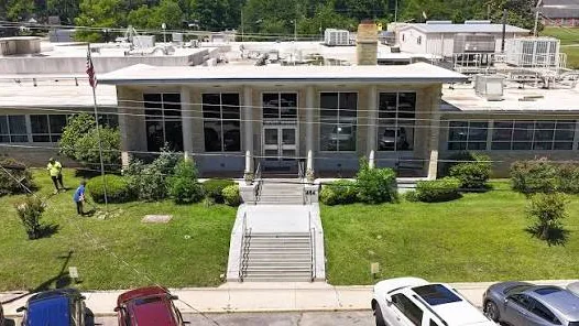 Front of the Bradley County Medical Center: a long one-story light-colored building with a white-roofed central entrance and steps, the number 444 on the wall beside the steps, a flagpole, and two people on the lawn.