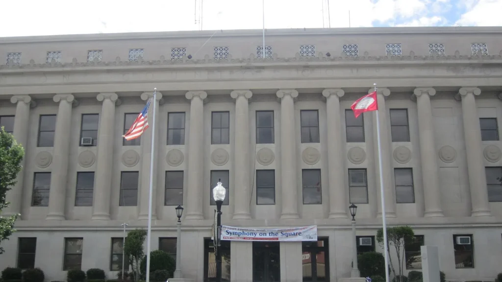 Union County Courthouse in El Dorado, Arkansas: a light stone building with a long row of tall columns and the words UNION COUNTY COURTHOUSE carved above them, with U.S. and Arkansas flags out front.