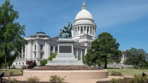 The white-domed Arkansas State Capitol in Little Rock, seen from the lawn under a clear blue sky.