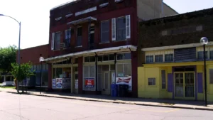 A row of older brick storefronts on a corner in downtown Dermott, Arkansas, in bright sunlight.