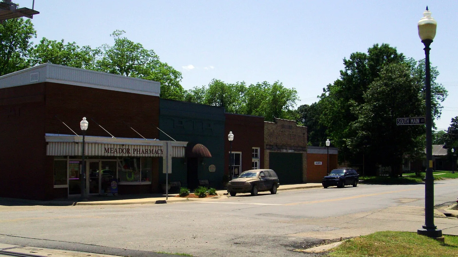 A corner of Main Street in downtown Dumas, Arkansas, with a row of one-story storefronts including Dumas Pharmacy.