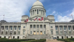 The Arkansas State Capitol in Little Rock, a white neoclassical building with a central dome and U.S. and Arkansas flags in front.