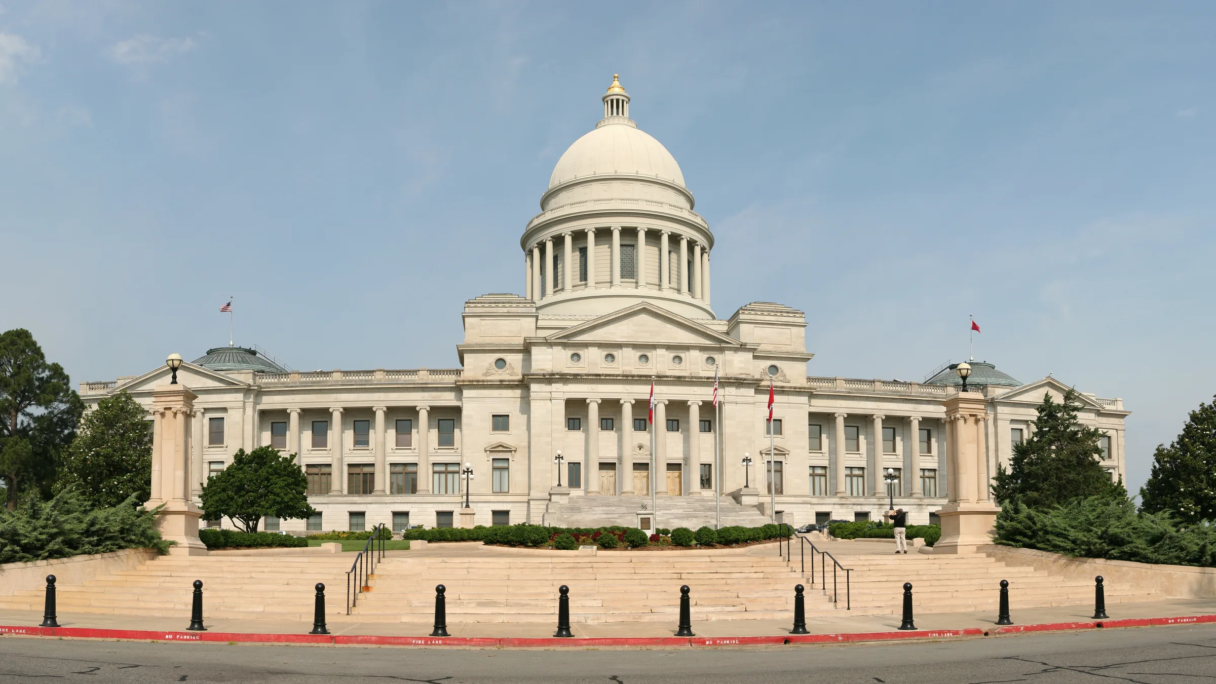 The Arkansas State Capitol in Little Rock seen wide across its lawn, a long white neoclassical building with a central dome.