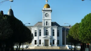The front of the white Jefferson County Courthouse in Pine Bluff, Arkansas, with its clock tower and gold dome, framed by trees under a blue sky.