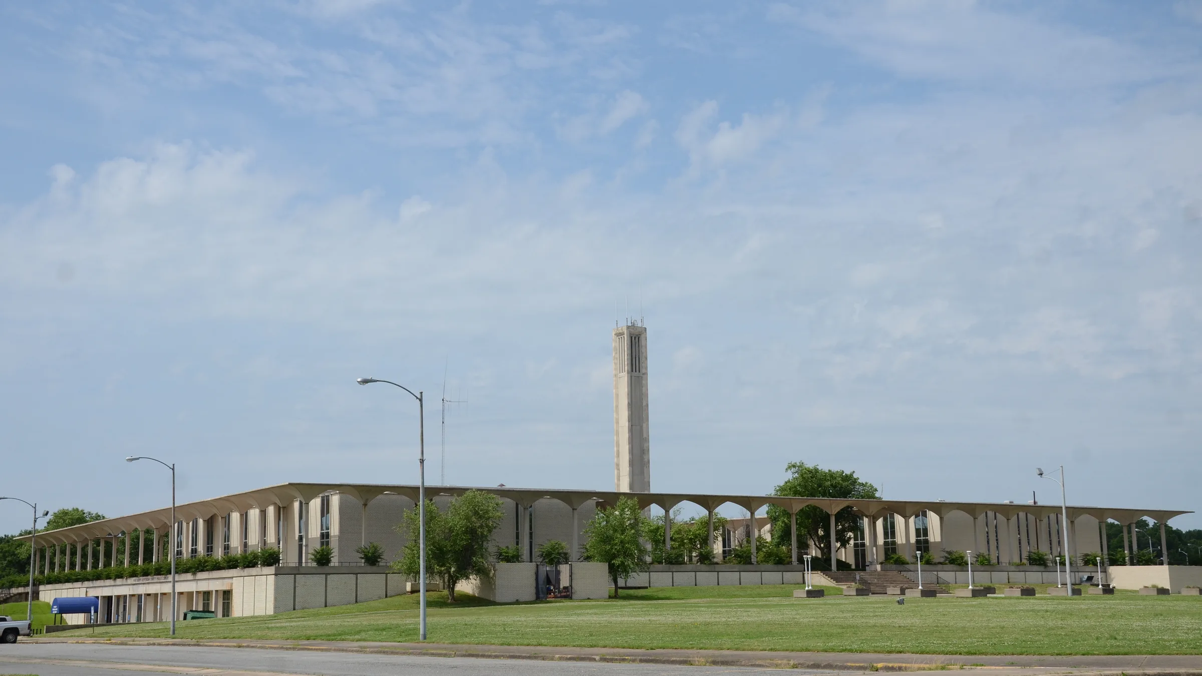 The Pine Bluff Civic Center in Arkansas, a long light-colored building with a colonnade of slender pillars and a tall square tower rising behind it, across a green lawn.