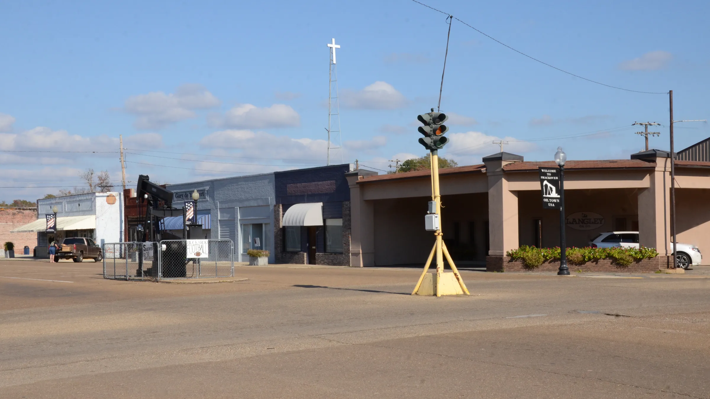The Smackover Historic Commercial District in Arkansas, a wide intersection with low commercial buildings, a vintage traffic signal and an oil pumpjack.