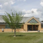 Gibson University Center on the University of Arkansas at Monticello campus, a tan building with an angled metal roof and the center name on the front.