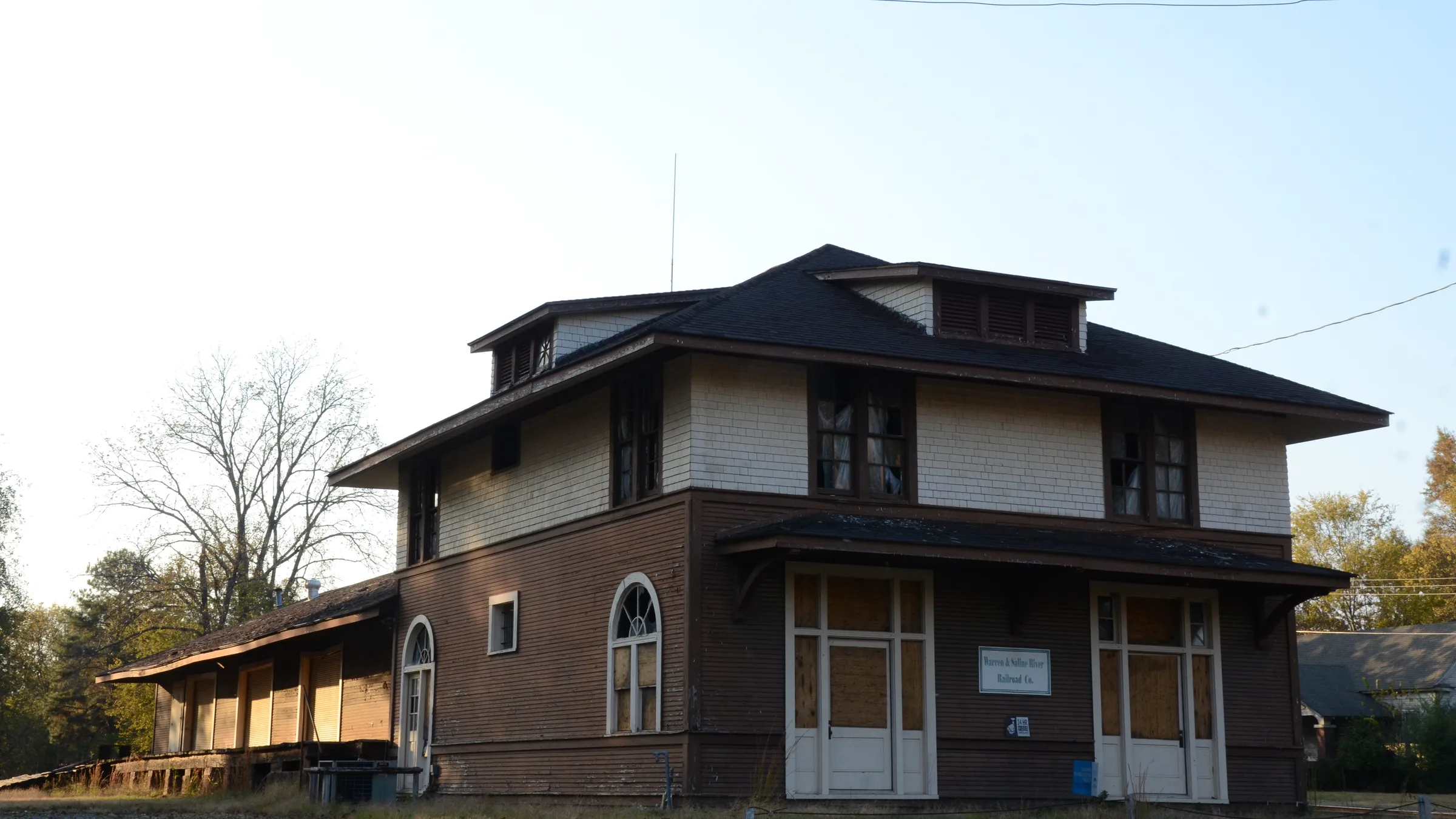 The historic railroad depot in Warren, Arkansas, a two-story building with brown siding, an upper floor of off-white shingles, a hipped roof with dormers and a long loading-platform wing.